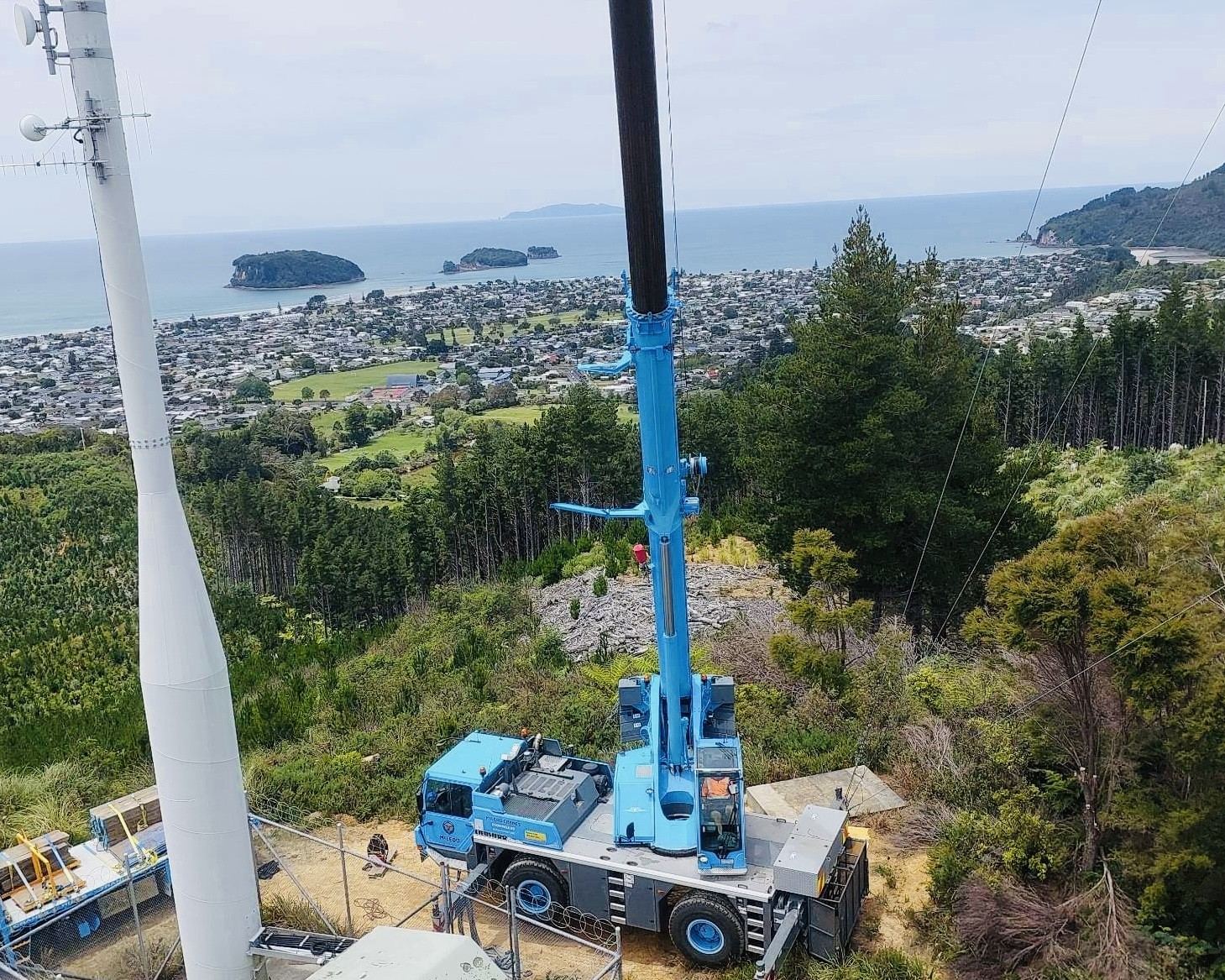 Mobile crane erecting a cell phone tower above a coastal town